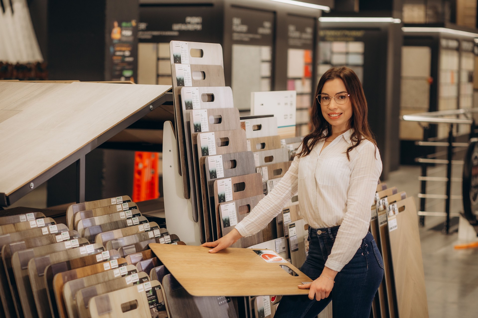 in hardware department,female buyer carefully examines laminate sample.Woman chooses flooring material.reflective girl stands near showcase with wood finishing materials.waiting seller s consultation