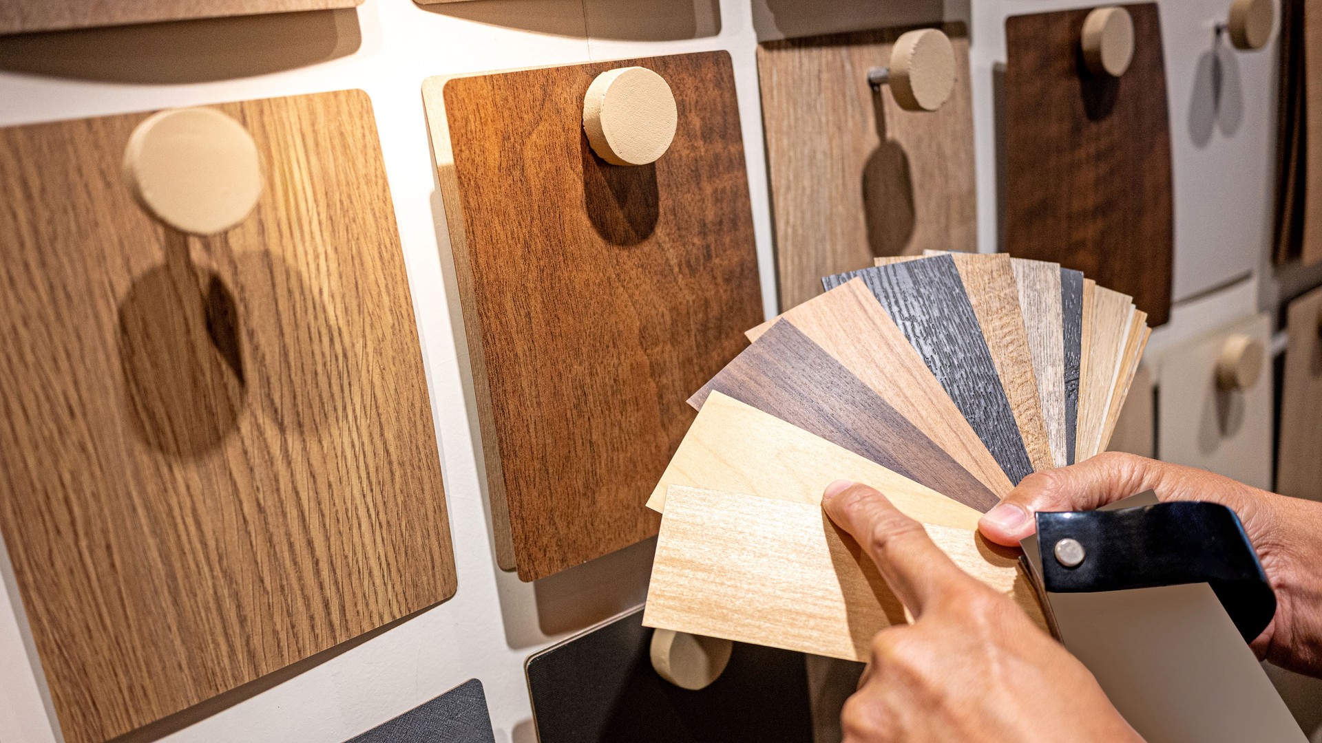 Designer hand pointing at sample of wood laminated from natural collection in material showroom. Choosing wooden veneer texture or MDF board swatch fan set for interior finishing or furniture design